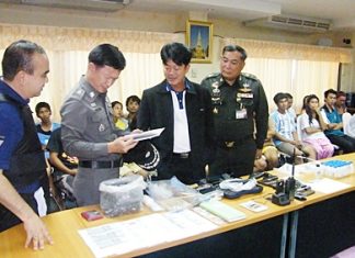 Chonburi Gov. Wichit Chatpaisit and high ranking police officials pour over the confiscated paraphernalia, as those arrested sit and wait processing behind them.